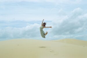woman in white dress jumping on brown sand during daytime